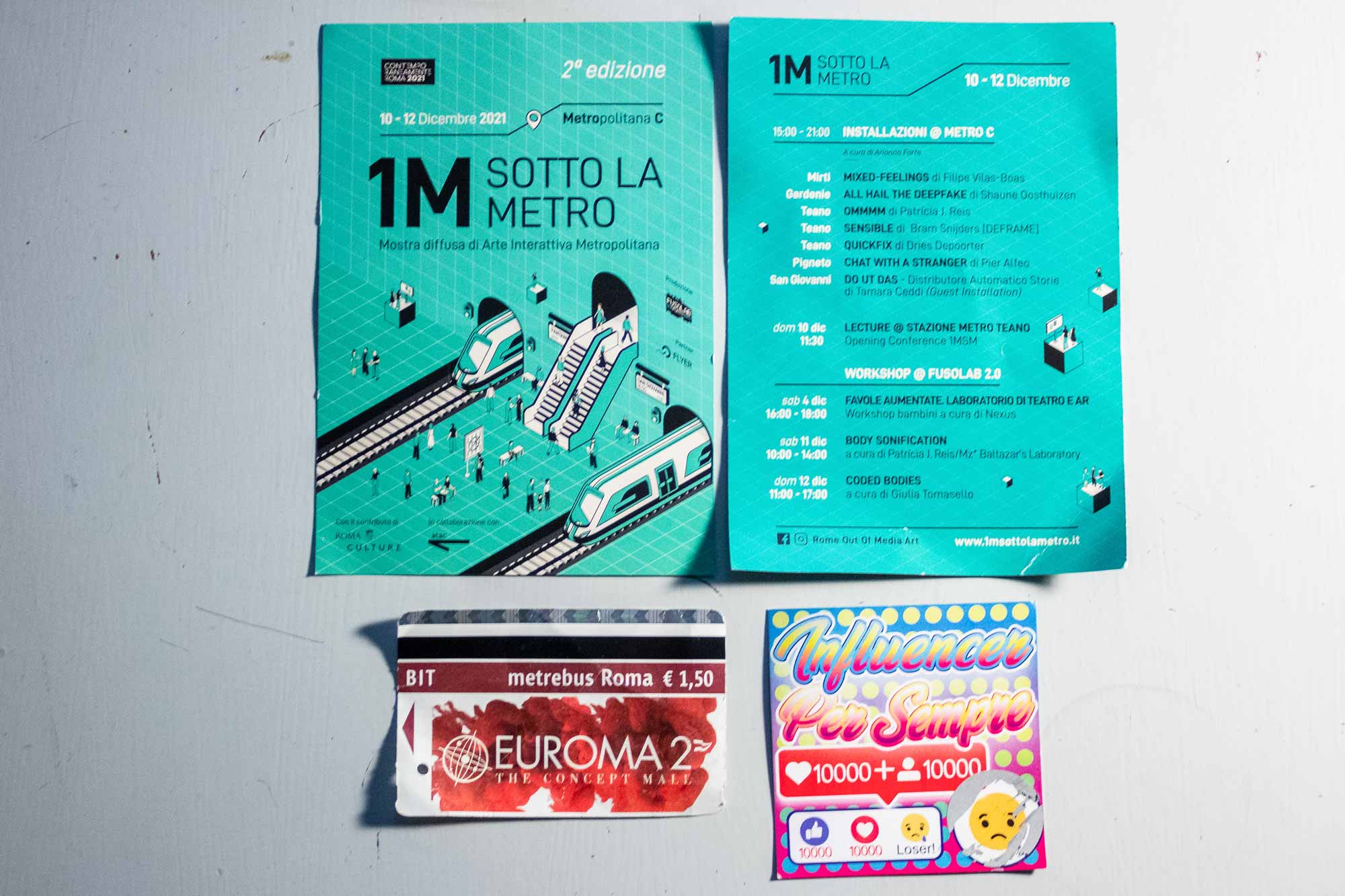Mostra diffusa di arte interattiva metropolitana, 1M sotto la Metro è un progetto site e time specific volto a coinvolgere il pubblico in un’esperienza innovativa che, attraverso l’arte contemporanea e le nuove tecnologie, permetta una differente interpretazione degli spazi diffusi della città, nello specifico le fermate della linea C della metropolitana romana. Una mostra diffusa, in cui opere di arte interattiva animano la rete metropolitana cambiando la relazione con un ambiente in cui passiamo distrattamente tutti i giorni, un “non-luogo” da attraversare, fatto di attese, corse e che ci proietta e ci trasporta in altri luoghi. Le stazioni della Metro C oltre ad essere dei “passaggi” per la prossima fermata, diventano “gate” su nuovi punti di vista sul mondo: nuove fermate nell’immaginario del futuro e sul presente. 1MSM è una mostra diffusa di opere di arte interattiva, ossia progetti in cui è fondamentale la partecipazione attiva dello spettatore. Prendendo in considerazione la qualità artistica del dialogo tra il livello di contenuto e il livello di interazione, sono predilette le installazioni e i progetti di arti digitali e new media. A livello tematico ci interessa affrontare una riflessione sui limiti del tempo presente – in riferimento alla situazione sociopolitica, ai risvolti della diffusione delle nuove tecnologie, al rapporto esseri umani-natura, ai sogni e necessità condivisi attualmente a livello globale. METRO C SAN GIOVANNI “DO UT DAS – DISTRIBUTORE AUTOMATICO STORIE 2.0” DI TAMARA CEDDI DO ut DAS è un’installazione site specific che viene azionata dall’inserimento di un biglietto o di un abbonamento Atac e che, una volta validato il titolo di viaggio, restituisce una storia/poesia stampata su uno scontrino. L’interazione è duplice: la prima riguarda le storie che vengono inviate al sito della mostra 1MSM e raccolte in un database, la seconda è quella degli utenti della metro che fruiscono di queste storie tramite l’inserimento del titolo di viaggio. L’installazione è realizzata in collaborazione con I “Poeti der Trullo” e il loro Metroromanticismo, il movimento poetico che parte dal quartiere e dalla vita di tutti i giorni, in continua costruzione attraverso il dialogo con le persone. Il MetroRomanticismo è il Romanticismo nei contesti urbani e metropolitani in cui siamo cresciuti: il quartiere, la periferia, il sobborgo. La fabbrica abbandonata diventa la montagna infinita dei vecchi Romantici, le case popolari sono castelli e la fermata della metropolitana è la tenuta in campagna. Il MetroRomanticismo appartiene alla strada e la città è concepita come un immenso foglio bianco su cui fare poesia. Do ut das è un invito a ritagliarsi una piccola frazione di tempo disconnessi dai dispositivi elettronici per dedicarlo alla poesia. Una delle migliori in condizioni di disprezzo e di difficoltà conosci il vero prezzo della tua identità. in condizioni di paura e di disillusione, stretto in quattro mura da’i spazio alla creazione. in condizioni di follia mista ad abbandono fai crescere poesia che suona come tuono. in condizioni di esclusione, di rabbia e isolamento assisti all’esplosione di forza e sentimento. I POETI DER TRULLO METRO C PIGNETO “CHAT WITH A STRANGER” DI PIER ALFEO “Chat with a stranger” è l’installazione interattiva site specific del sound artist pugliese Pier Alfeo, progettata espressamente per la mostra 1MSM. L’opera riflette sull’assenza di comunicazione e la disindividualizzazione tipiche di quelli che possono essere definiti “non-luoghi”, ambienti di transizione e temporanei, come la metro appunto. “Chat with a stranger” vuole restituire la necessità di instaurare una relazione e una comunicazione tra chi transita in questi spazi. Invita il visitatore a prendere parte a una una chat con i visitatori precedenti, senza necessariamente conoscerli. I testi e la presenza fisica di tutti coloro che hanno partecipato a questa conversazione aperta, generano una composizione di luce e di suoni che riempie lo schermo man mano che i contributi aumentano. Sono visualizzati come informi energie termiche che fluiscono e percepibili come suoni avvolgenti, morbidi e aggreganti. METRO C TEANO “SENSIBLE” DI BRAM SNIJDERS (DEFRAME) “Sensible” si interroga sul dialogo tra spazio fisico e digitale, sulla consistenza del primo in opposizione alle impercettibilità del secondo e sulla nostra capacità e abilità di abitare e agire questi ambienti. Nello specifico, l’opera indaga la capacità di percepire una superficie virtuale costruita di materia digitale all’interno di uno spazio fisico. Solo quando un oggetto o una persona si posizionano in corrispondenza delle coordinate di una soglia virtuale – questa si rivela nello spazio fisico e diventa percepibile attraverso manifestazioni istantanee di luce e suono. “Sensible” è il risultato di un’esplorazione delle moderne tecnologie combinate con la conoscenza open source applicata e l’interazione umana. “OMMMM” DI PATRICIA J. REIS OMMMM”è un’opera che stimola il sistema sensoriale tattile del visitatore, inducendo il suo rilassamento psicofisico attraverso la produzione di semplici dati biometrici, come l’emissione del suono emblematico del relax, “ommm”. L’installazione interattiva è un appello alla sensorialità del visitatore in un ambiente intimo e sensuale e ha le sembianze di una poltrona massaggiante. Invita i partecipanti a impegnarsi fisicamente e corporalmente, sperimentando sensazioni aptiche derivanti dai dati raccolti dai suoni generati dal proprio corpo. Recitando i mantra Om e Am,o producendo suoni simili, si attivano e si gestiscono i motori a vibrazione all’interno della sedia . Il suono viene quindi tradotto in un “massaggio” del corpo e ne modula l’intensità e la durata. “QUICK FIX” DI DRIES DEPOORTER “Quick Fix “ è un’installazione interattiva che propone una “soluzione rapida” alla necessità di gran parte della popolazione contemporanea: quella di raggiungere la popolarità sui social network. L’opera è un distributore automatico che permette di comprare followers o likes su Instagram in pochi secondi. “Quick Fix” è facile da usare. Scegli il tuo prodotto, paga e inserisci il tuo nome utente di instagram. Riceverai i like o i followers solo pochi secondi dopo. Ovviamente gli account che ti mettono like o che iniziano a seguirti sono account falsi. Ogni ordine viene salvato in un database e viene salvato con la posizione della mostra, data, città, paese. La prima versione di “Quick Fix” è stata commissionata dal festival Pixelache nel 2019 a Helsinki ed è stata prodotta nello studio di Dries a Gand, in Belgio. METRO C MIRTI “MIXED FEELINGS” DI FILIPE VILAS-BOAS “Mixed Feelings” è un’installazione interattiva che trae ispirazione dalle emozioni identificabili sul nostro viso per comporre e improvvisare musica in tempo reale. Il dispositivo combina un sistema di riconoscimento facciale con una rete neurale addestrata a creare musica. In “Mixed Feelings”, si esplora il potenziale poetico del riconoscimento facciale utilizzando la rilevazione delle emozioni, o almeno delle espressioni che le compongono, come un input alla creazione musicale, laddove per l’ascoltatore sono sempre state intrinsecamente un output, il risultato dell’ascolto. L’ascoltatore si ritrova così analizzato, convertito e riprodotto in un infinito gioco di specchi musicale tra emozione umana e intelligenza artificiale. METRO C GARDENIE “ALL HAIL THE DEEPFAKE” DI SHAUNE OOSTHUIZEN “All Hail the Deepfake” è un’installazione audiovisiva interattiva che permette al pubblico di interpretare figure pubbliche di spicco e fargli eseguire azioni che altrimenti non eseguirebbero. L’opera è progettata per provocare una discussione sulla privacy dei dati, sull’uso dell’intelligenza artificiale e ovviamente sull’aumento del fenomeno del “deepfake” I deepfakes sono tecniche per manipolare o generare contenuti audiovisivi che sfruttano potenti tecnologie di apprendimento automatico (deep learning) e intelligenza artificiale, con un alto potenziale di inganno. La loro diffusione in contesti tipici della comunicazione social e online ha la conseguenza di offuscare il concetto di verità, incentivando fake news, truffe e crimini informatici. https://1msottolametro.it/