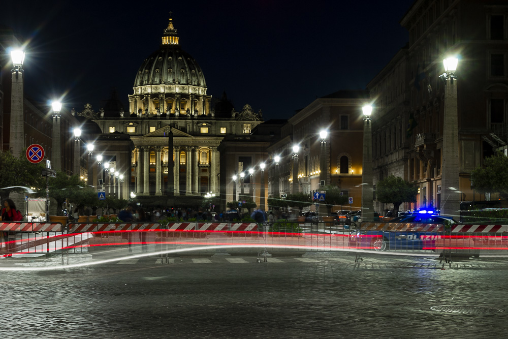 fotografia scattata a Roma, a San Pietro, verso viale della Conciliazione. I tempi sono lenti e si vedono le scie luminose dei fari posteriori e anteriori delle macchine. >Per il corso di fotografia urbana notturna con cavalletto